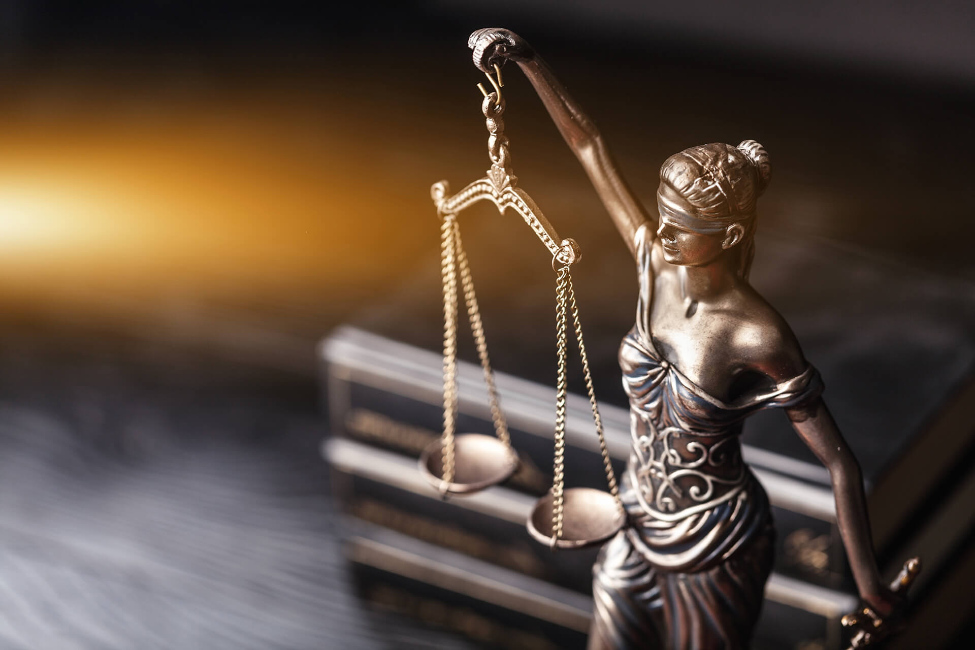 Statua della Giustizia bendata con una bilancia, accanto a libri di diritto